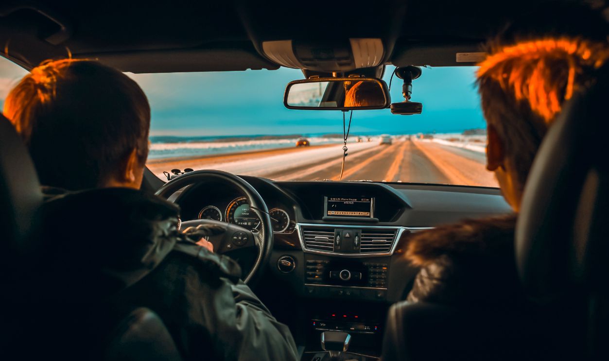 Interior view of a car driving down a snowy road at sunset with two people