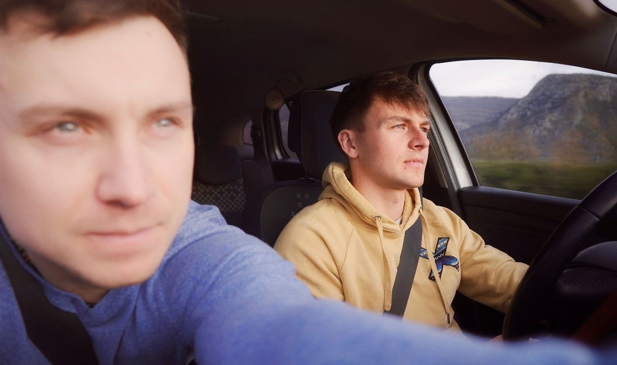 Two men driving a car through a scenic rocky landscape