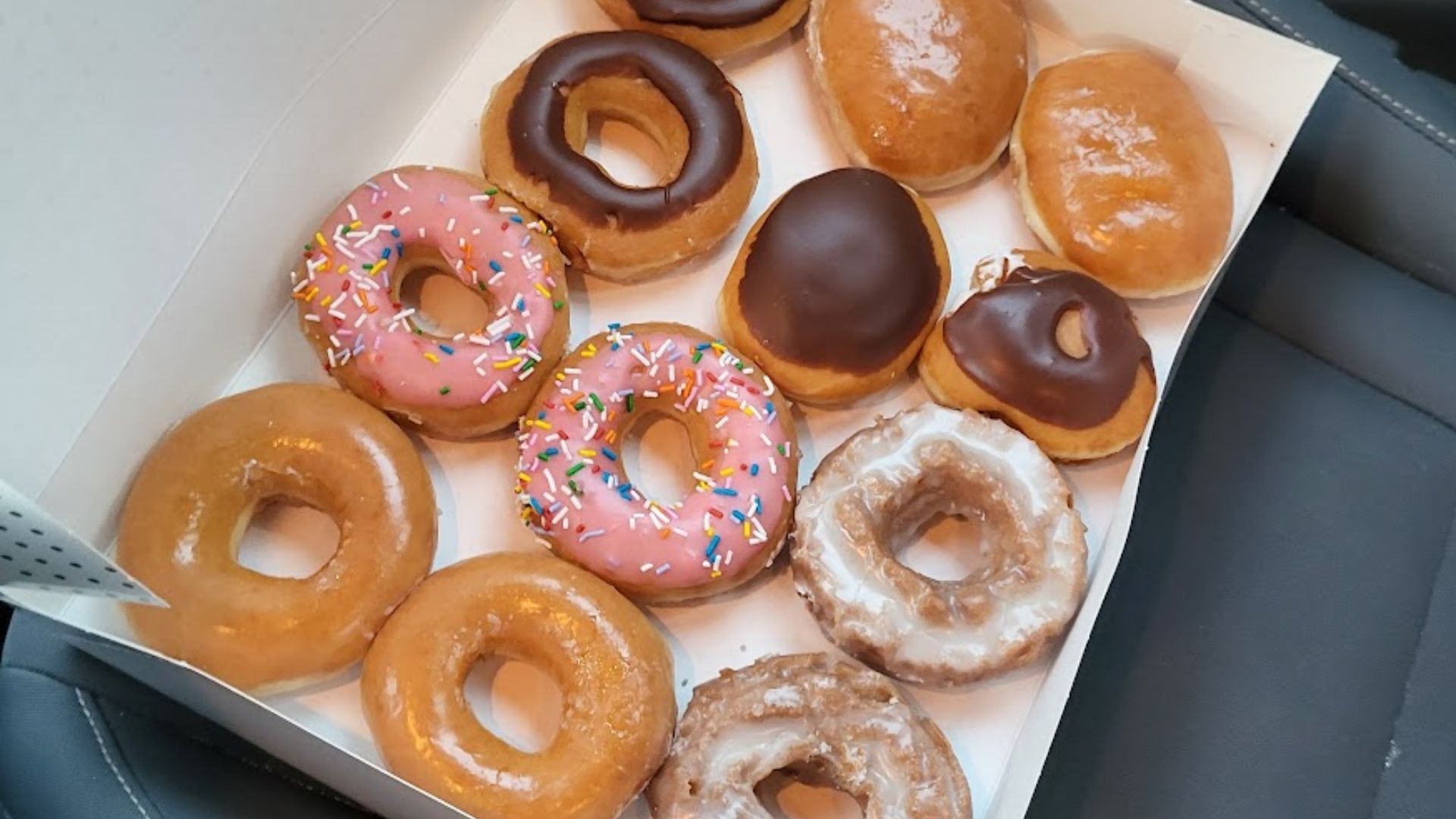 A dozen Krispy Kreme Donuts sitting on a car seat.