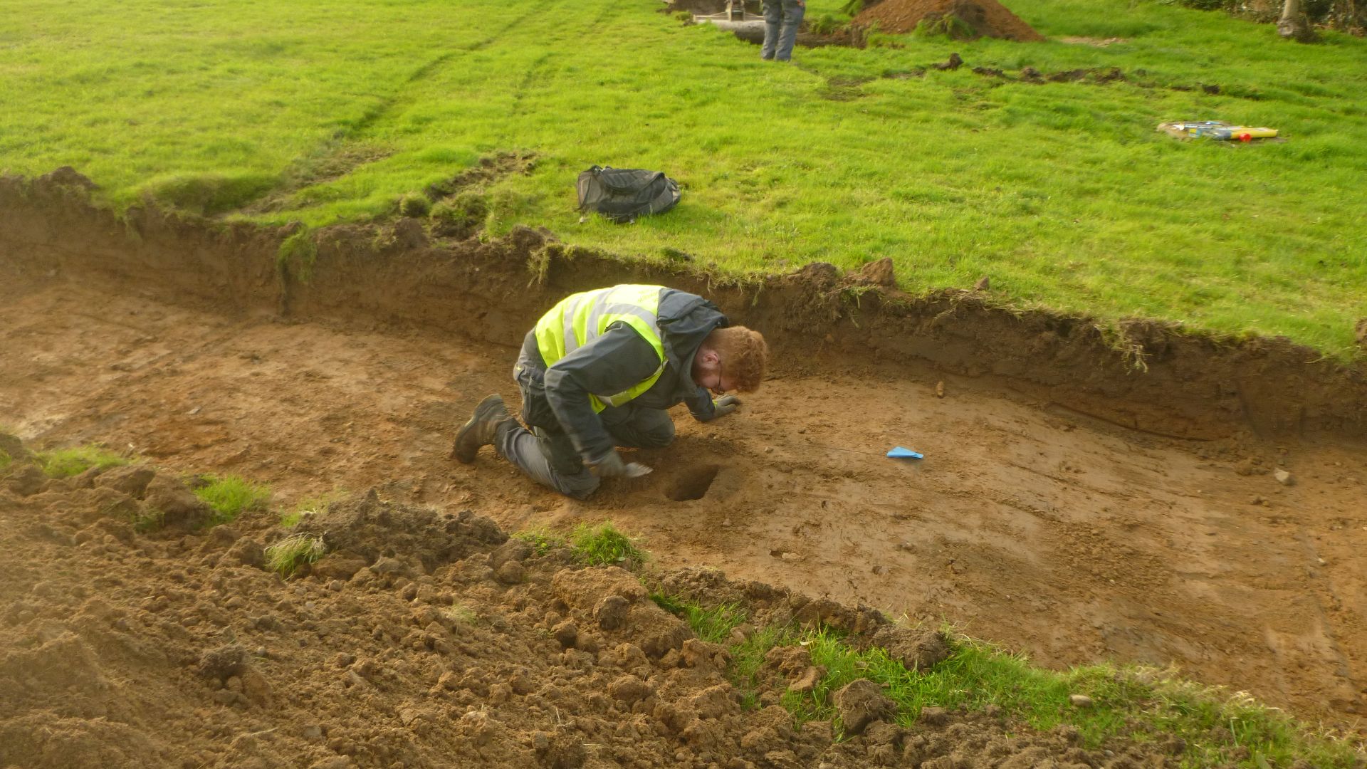 Archaeologist excavating a small feature in a trial trench at Cross Cottages, Cooks Hill, Boxted Cross, Essex, December 2021