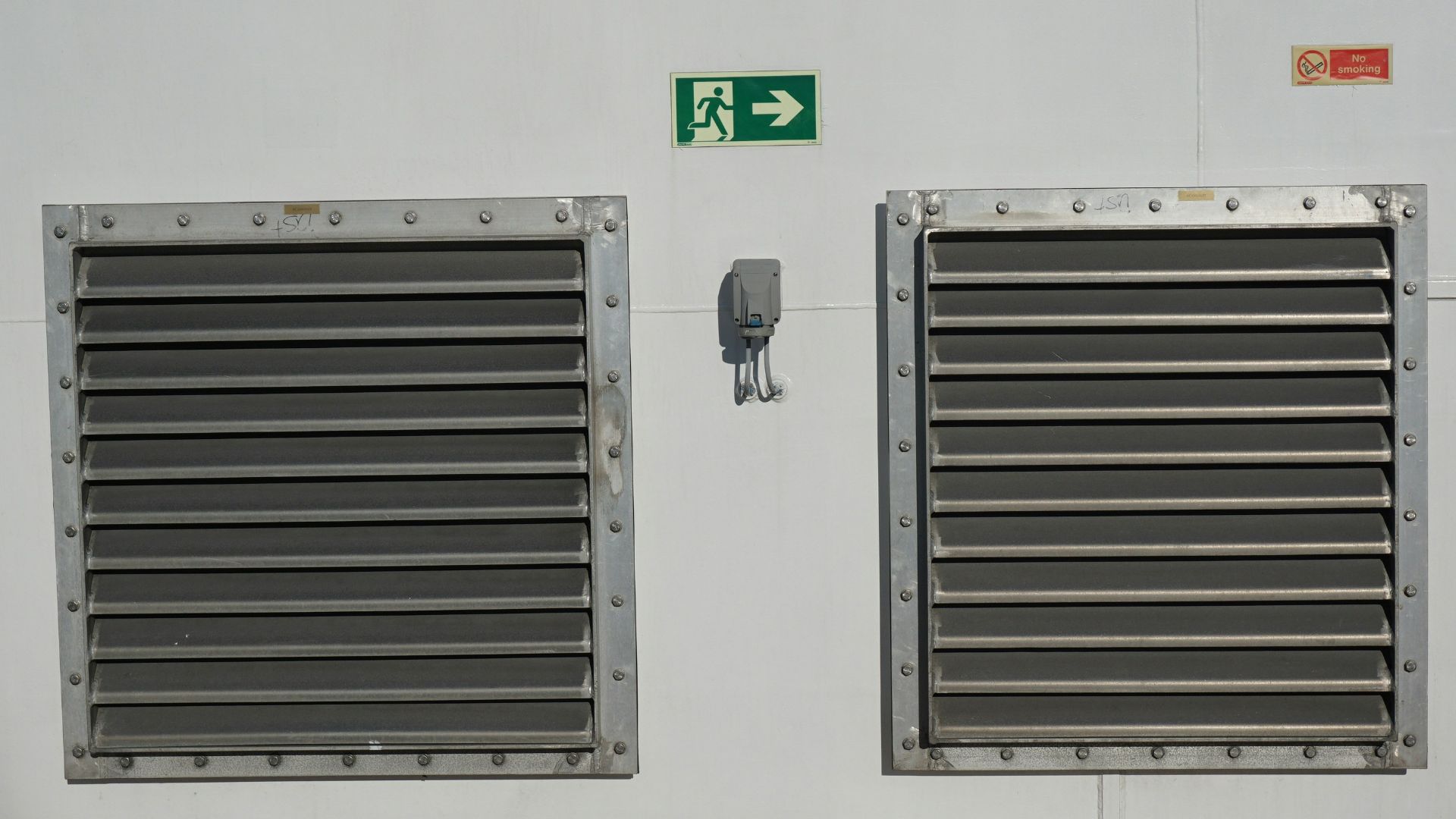 Two metal grates on a white wall with exit sign