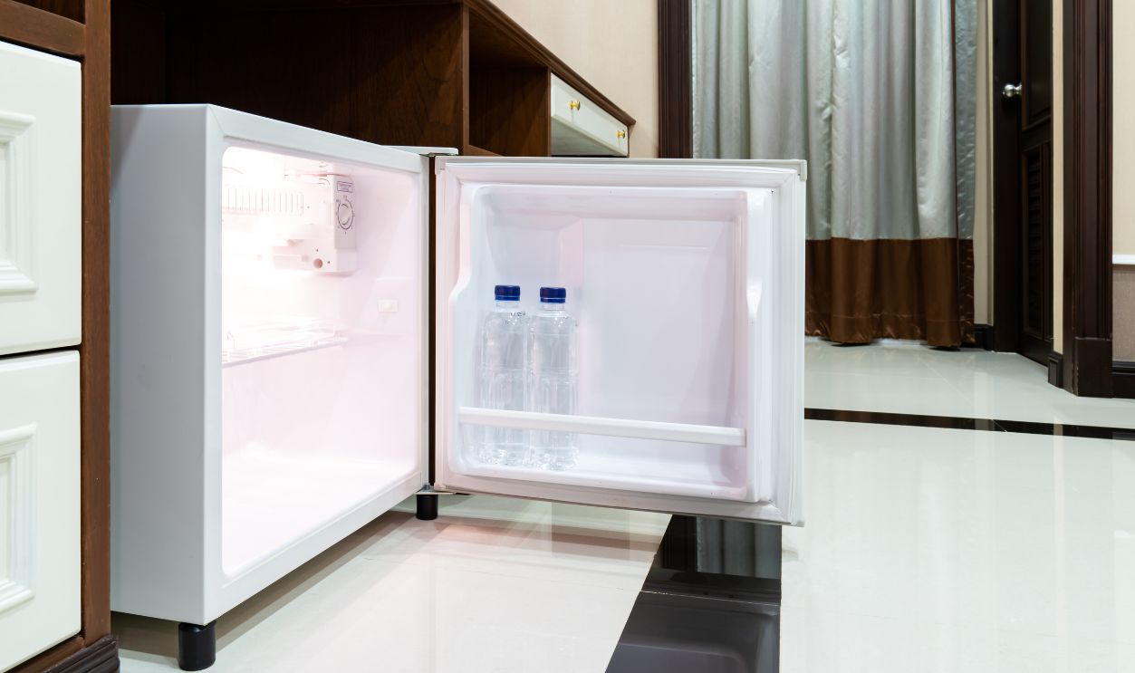 Refrigerator fridge mini size under the table counter with wooden desk beside it in hotel delux room.