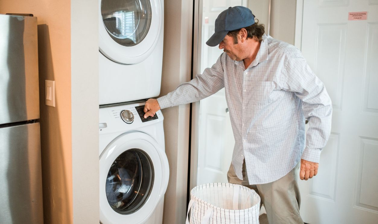A man places clothes in a washing machine at home, focusing on household chores