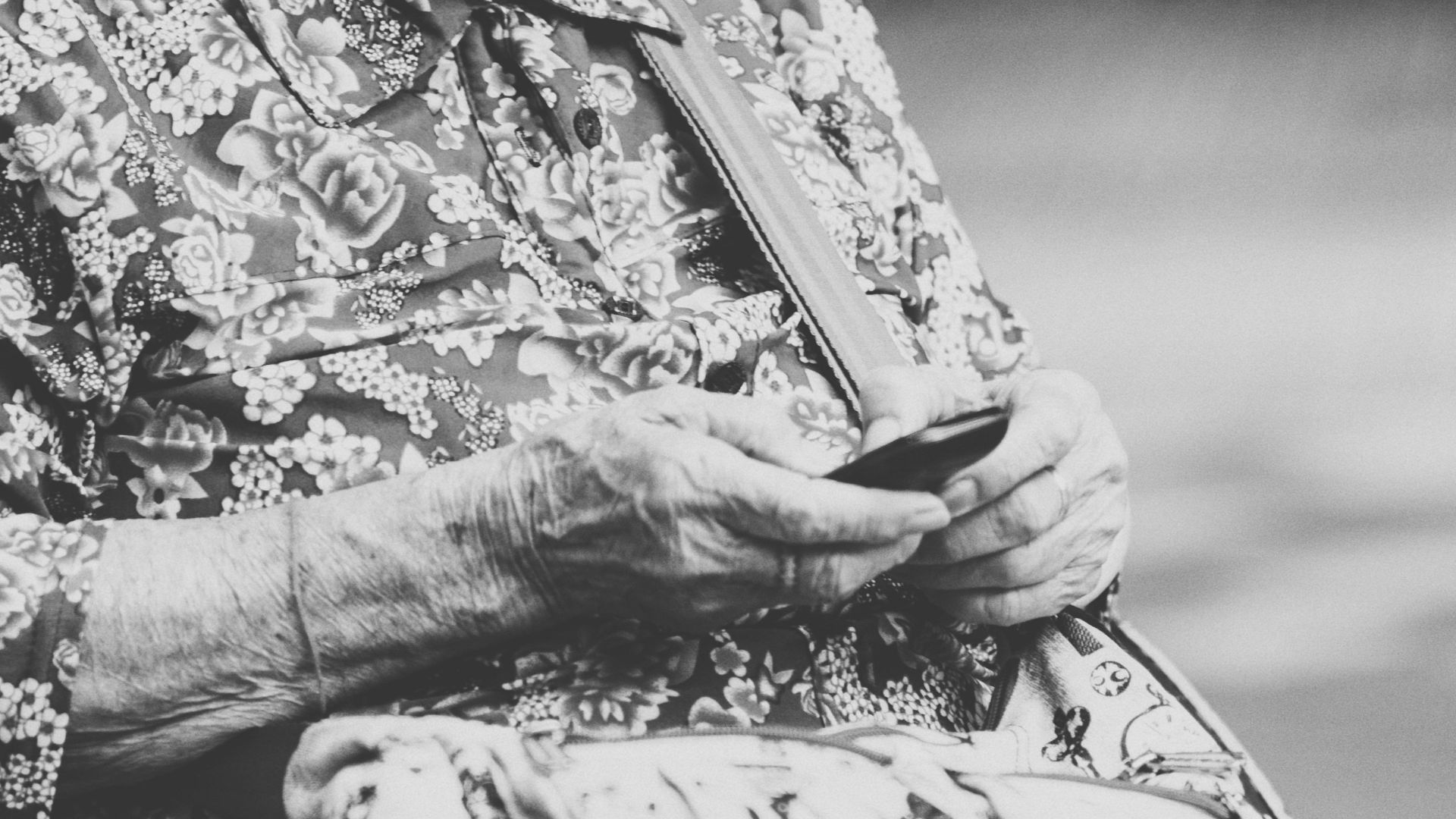 selective focus grayscale photography of woman using phone while sitting at bench