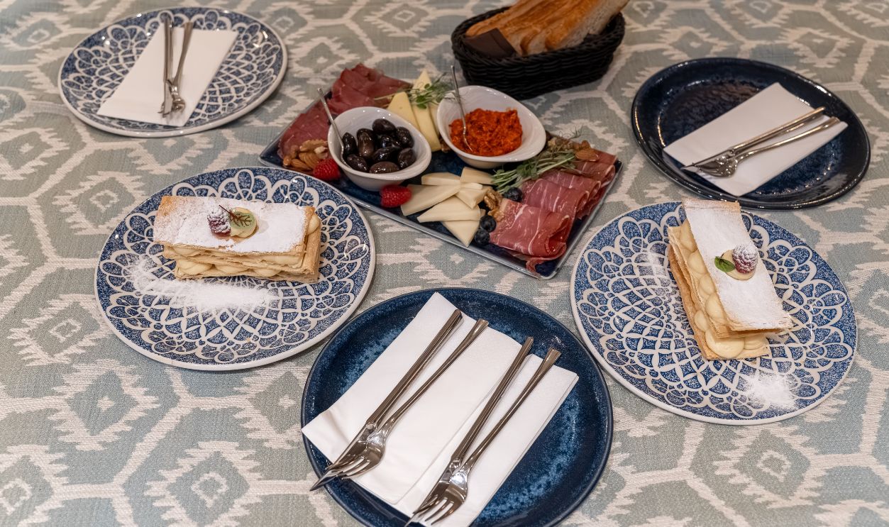 Elegant hotel room service meal arranged on a bed with layered desserts, charcuterie, cheese, olives, berries, bread and tableware. Luxury hospitality, romantic dinner and gourmet travel concept.