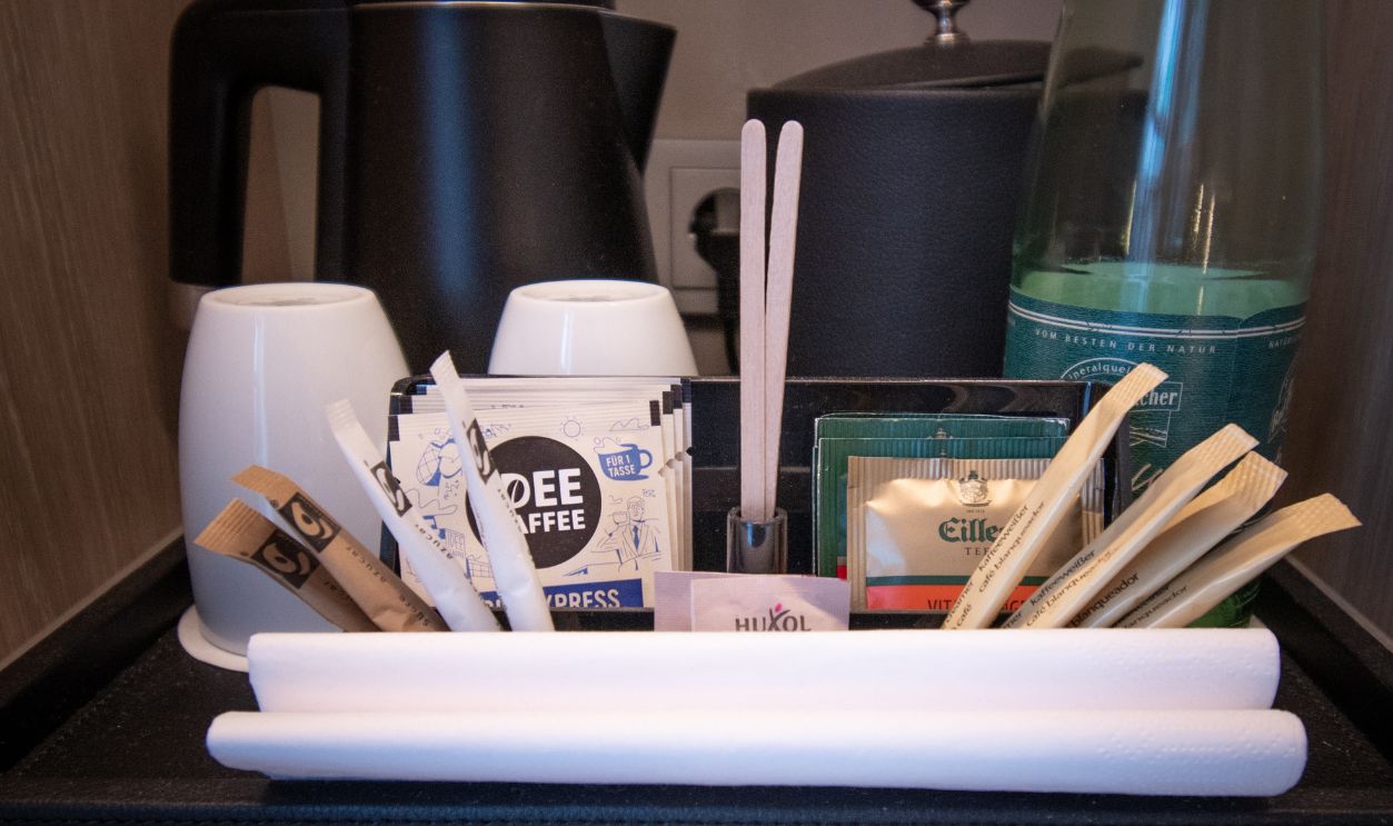 Berlin, Germany. February 12 2024. A neatly arranged hotel room beverage setup featuring coffee and tea options, a kettle, cups, and bottled water for guest convenience.