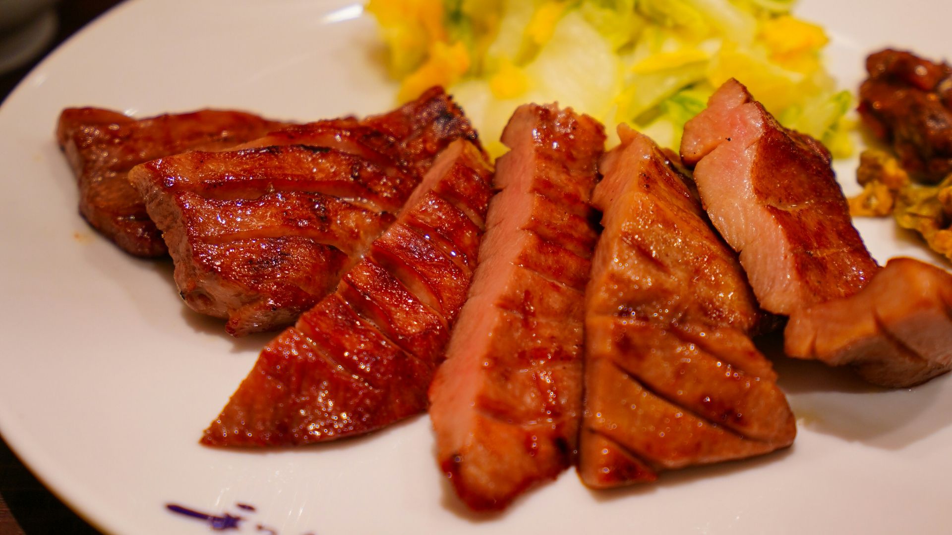 A plate of grilled sliced meat with a side salad