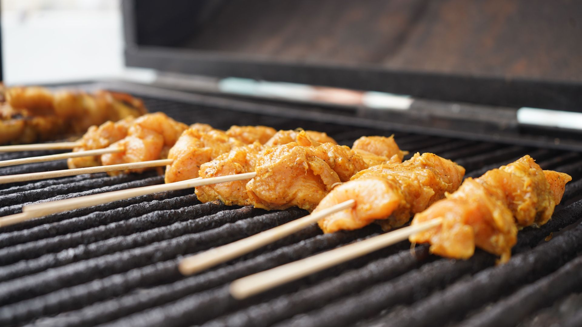 Close-up of juicy chicken skewers cooking on an outdoor grill.