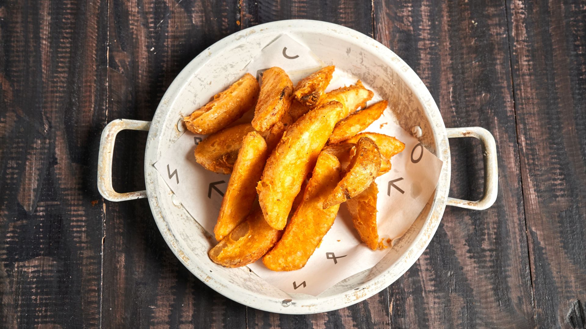 Golden crispy potato wedges served in a rustic white bowl on wood.