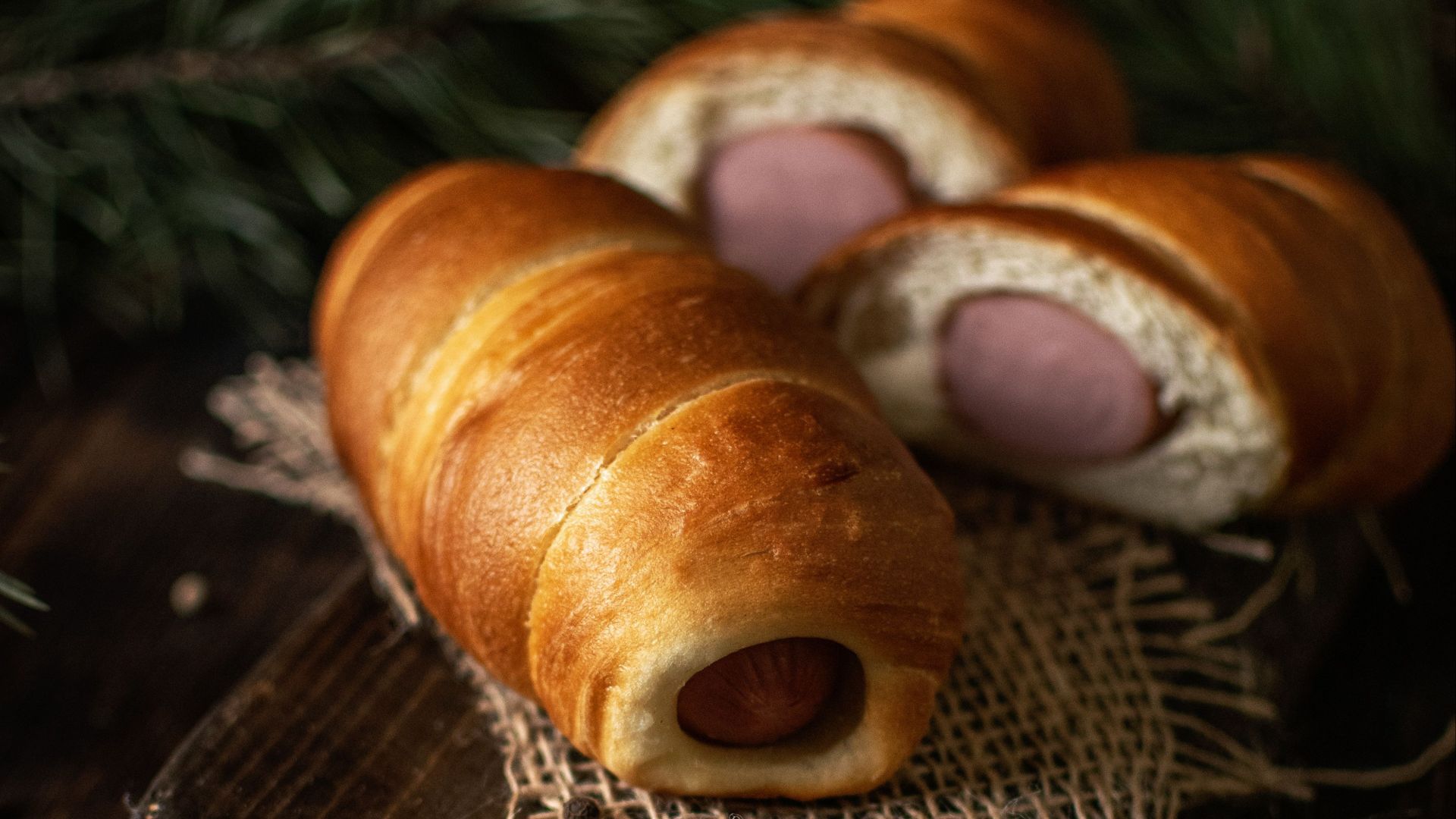 Gourmet hot dog rolls beautifully presented on a rustic wooden board, perfect for a savory meal.