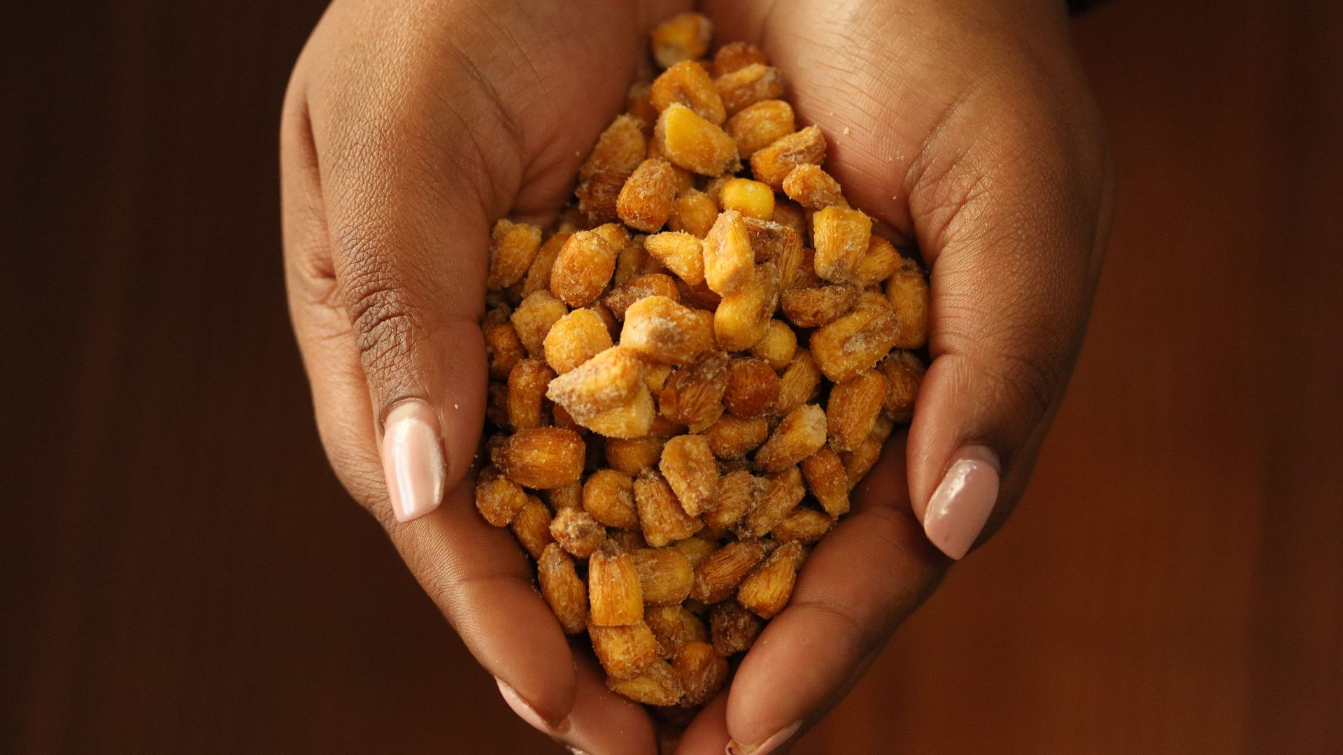 Close-up of hands holding crunchy roasted corn snacks on a wooden background.