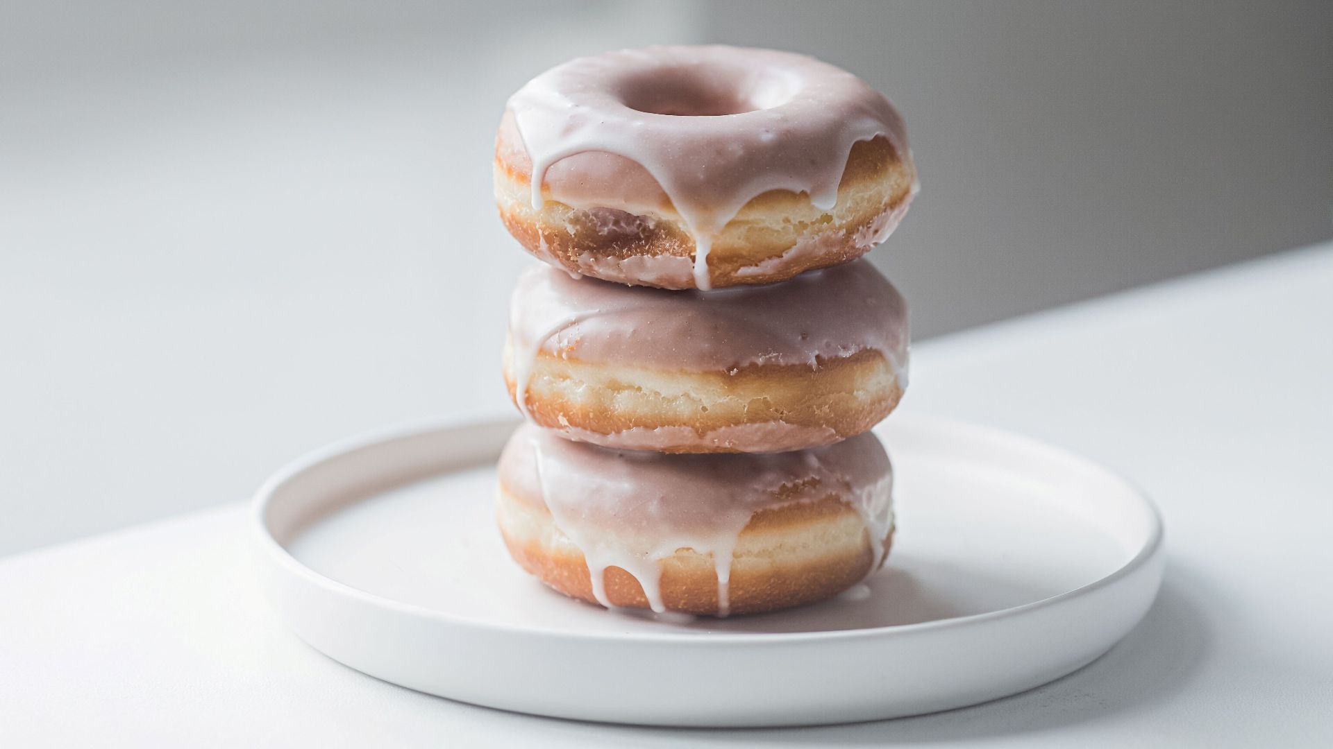A close-up shot of three stacked glazed donuts on a white plate indoors.