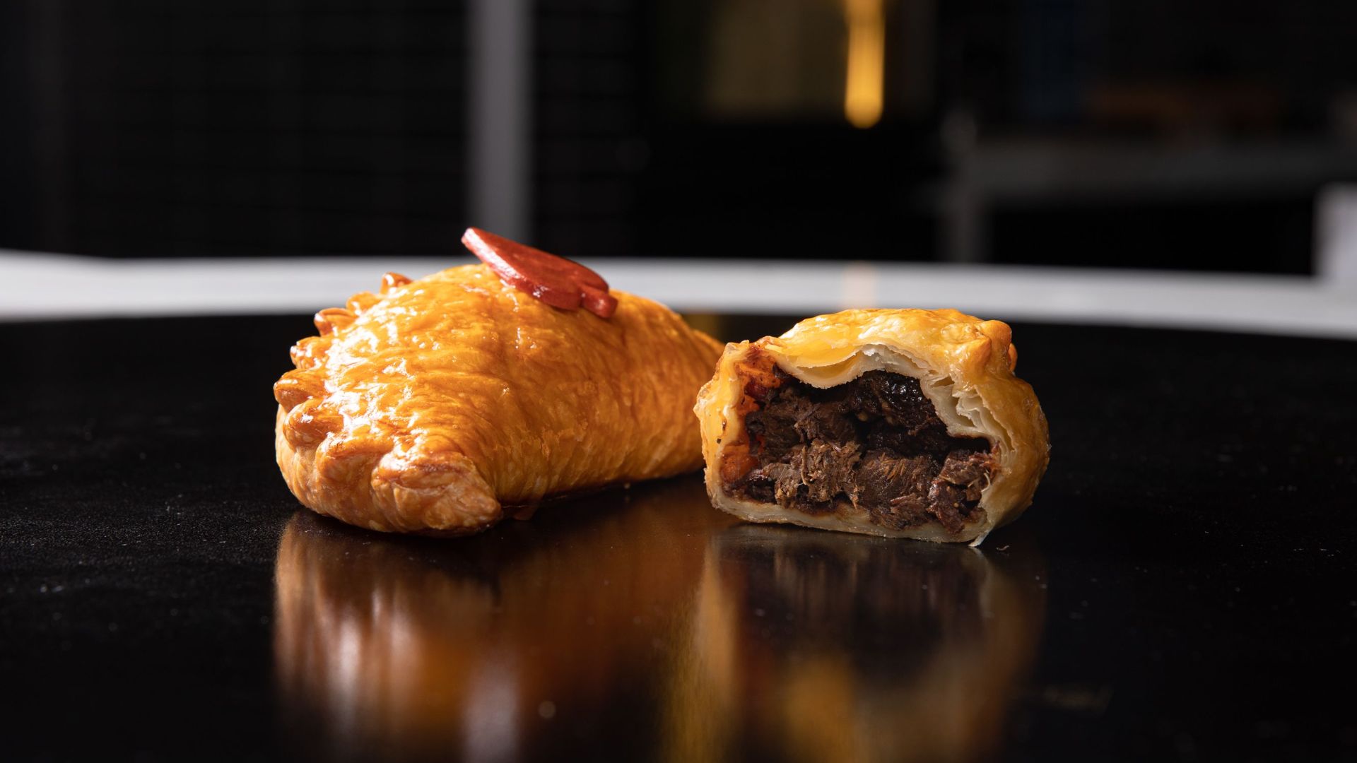 Appetizing close-up of a crispy, golden-brown pastry with a savory filling on a black surface.