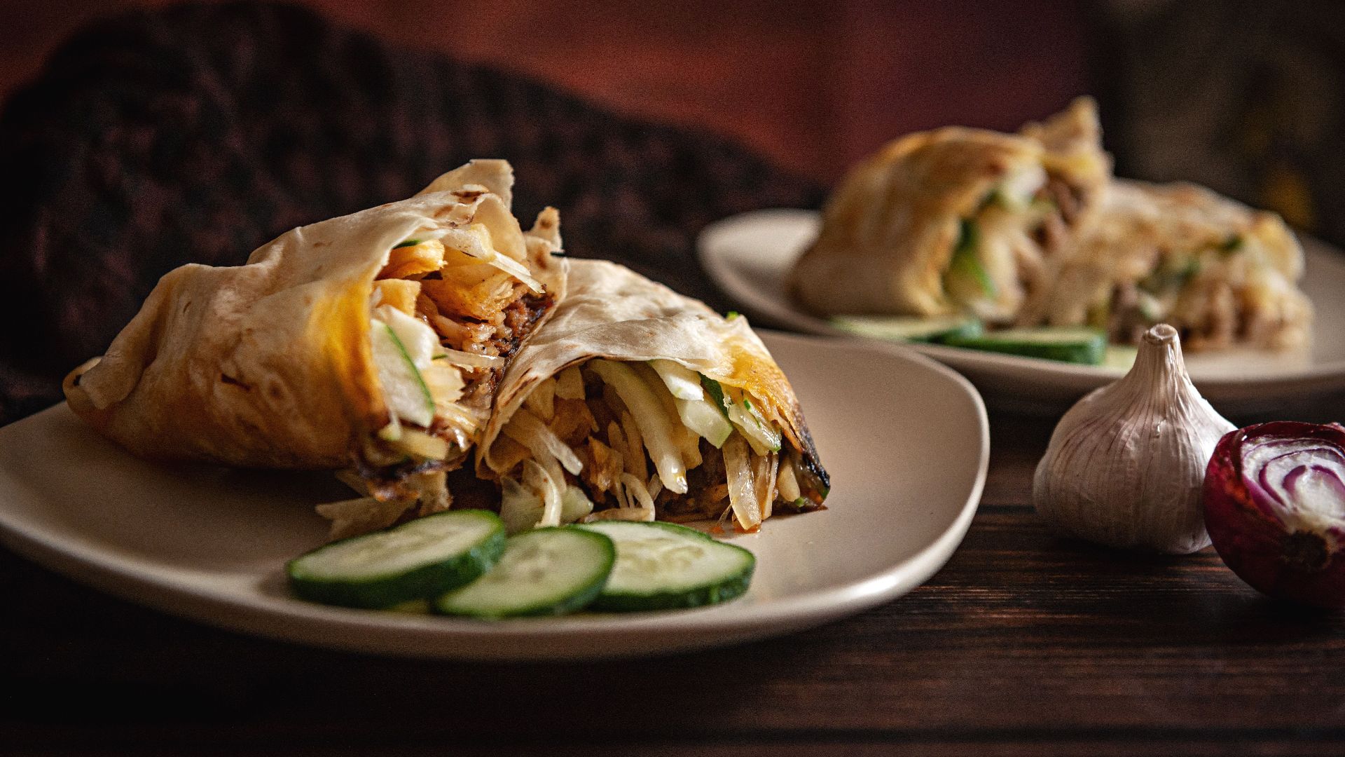 Close-up of shawarma wraps with cucumbers, garlic, and onions on plates.