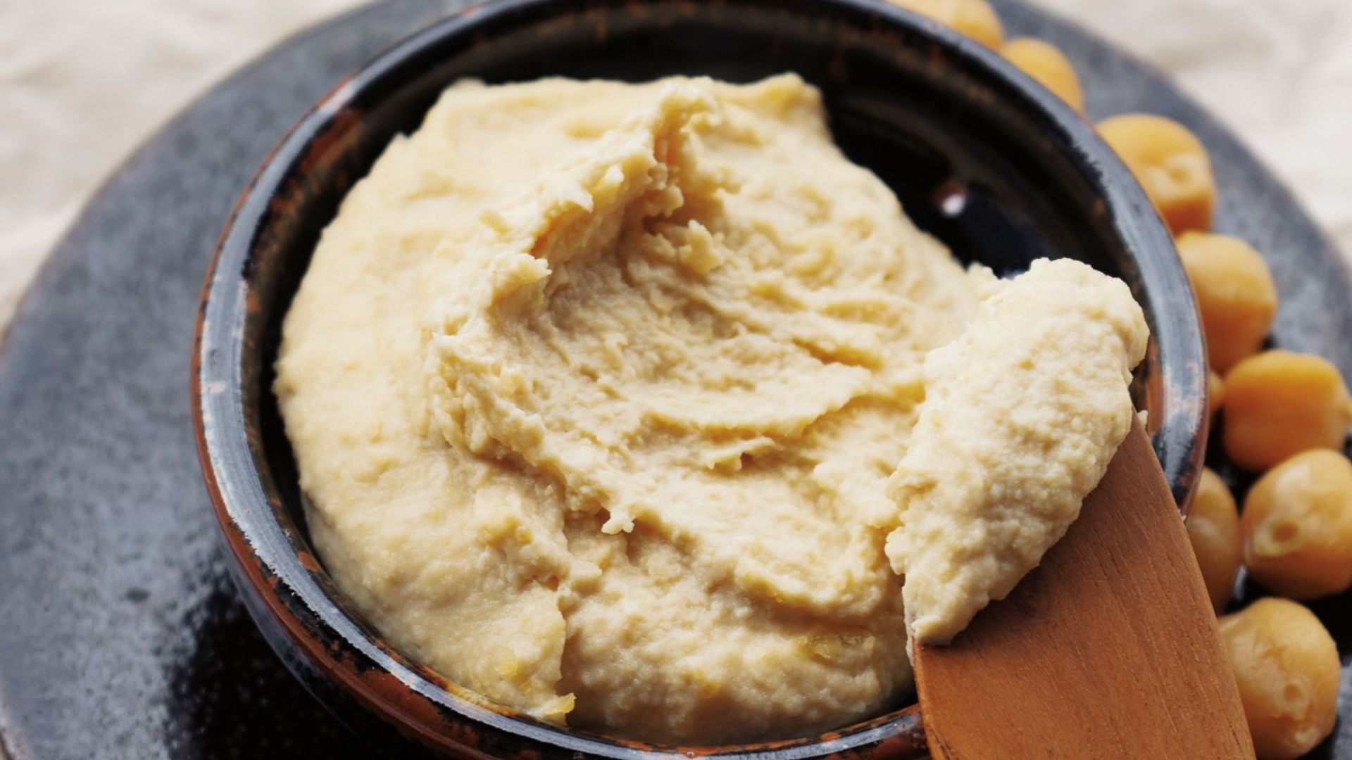Delicious homemade hummus in a bowl with scattered chickpeas on a rustic background.
