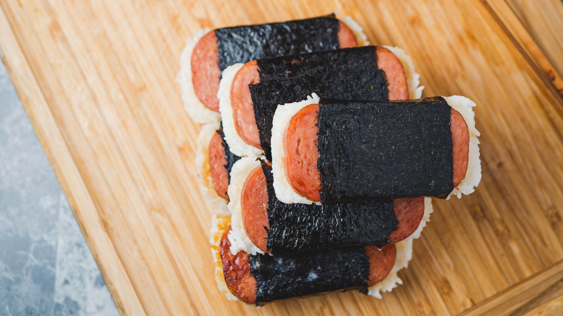 Appetizing spam musubi served with soy sauce on bamboo cutting board. Perfect for lunch delight.