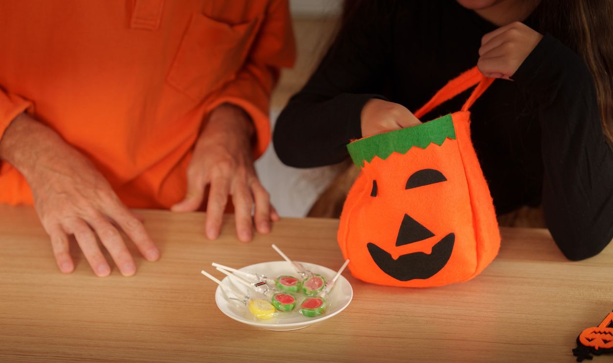 Child reaching into pumpkin treat bag for Halloween candy with parent