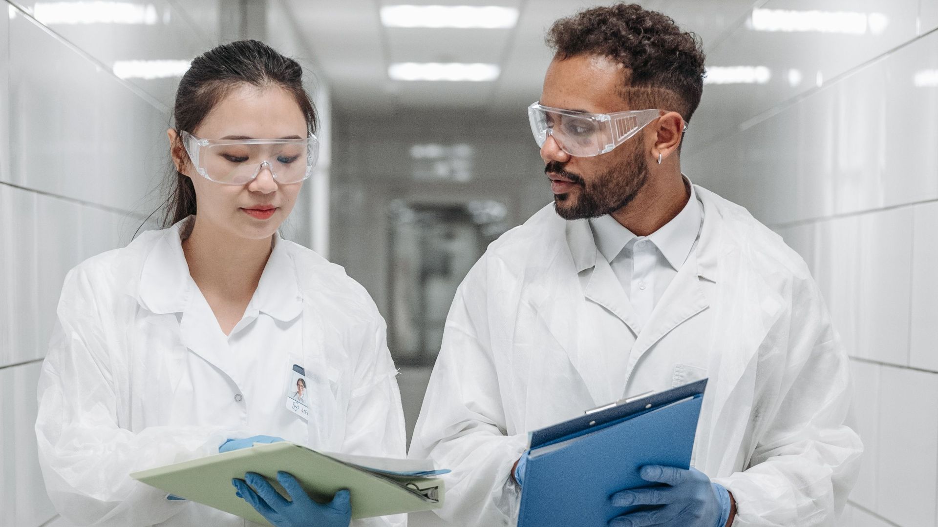 Two scientists in lab coats discussing research documents in a laboratory hallway.