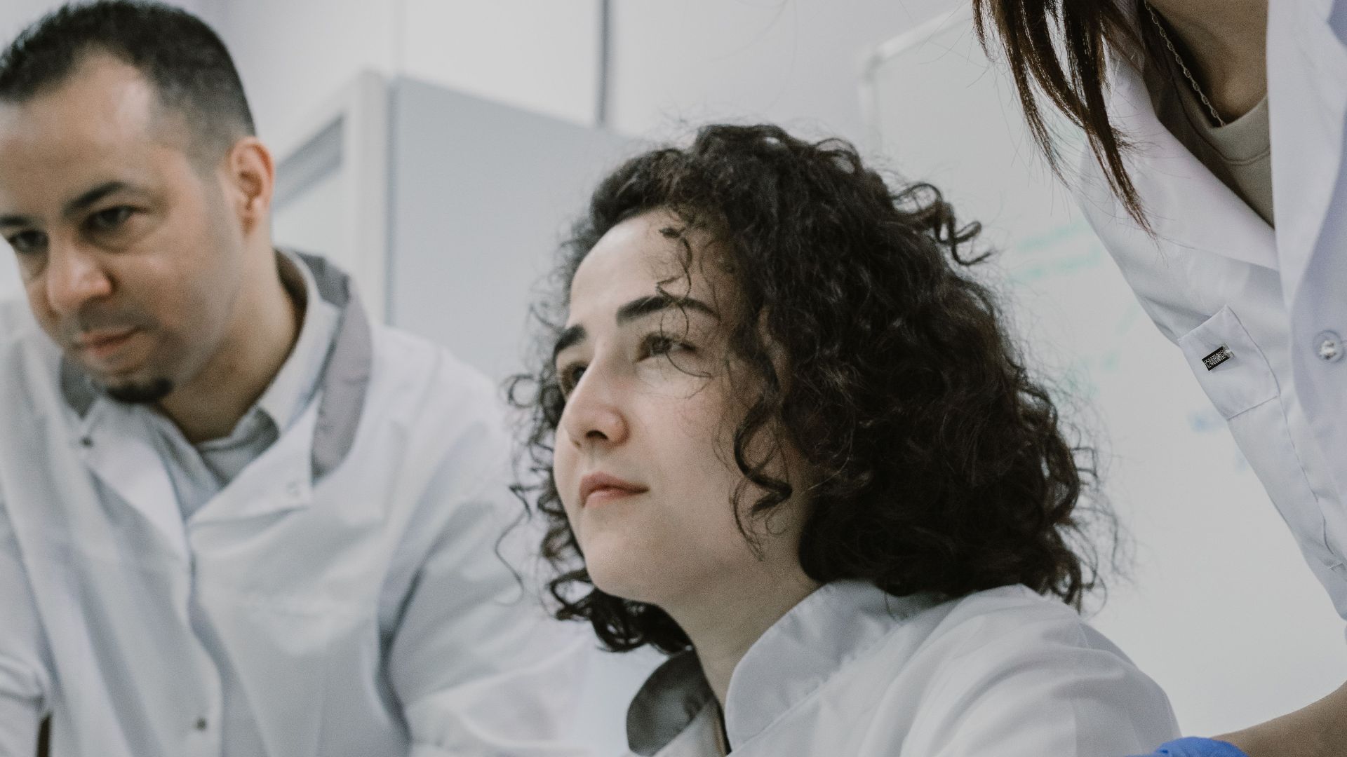 Three scientists wearing lab coats collaborate on research with books and computers in a modern laboratory setting.