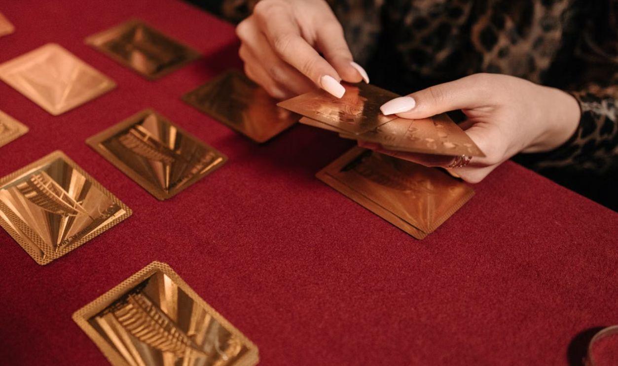 A close-up of hands holding gold cards while playing a card game on a red table. Perfect for gaming and leisure themes