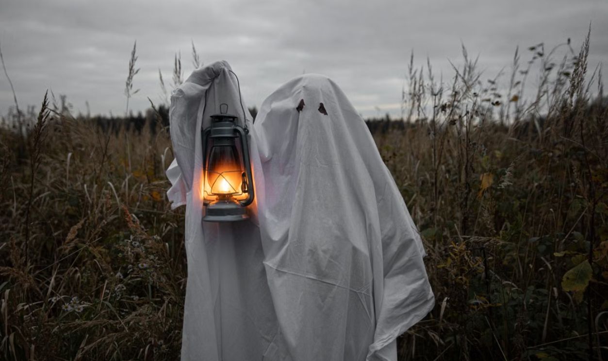 A ghostly figure holds a lantern in a dark, spooky field, embodying Halloween spirit