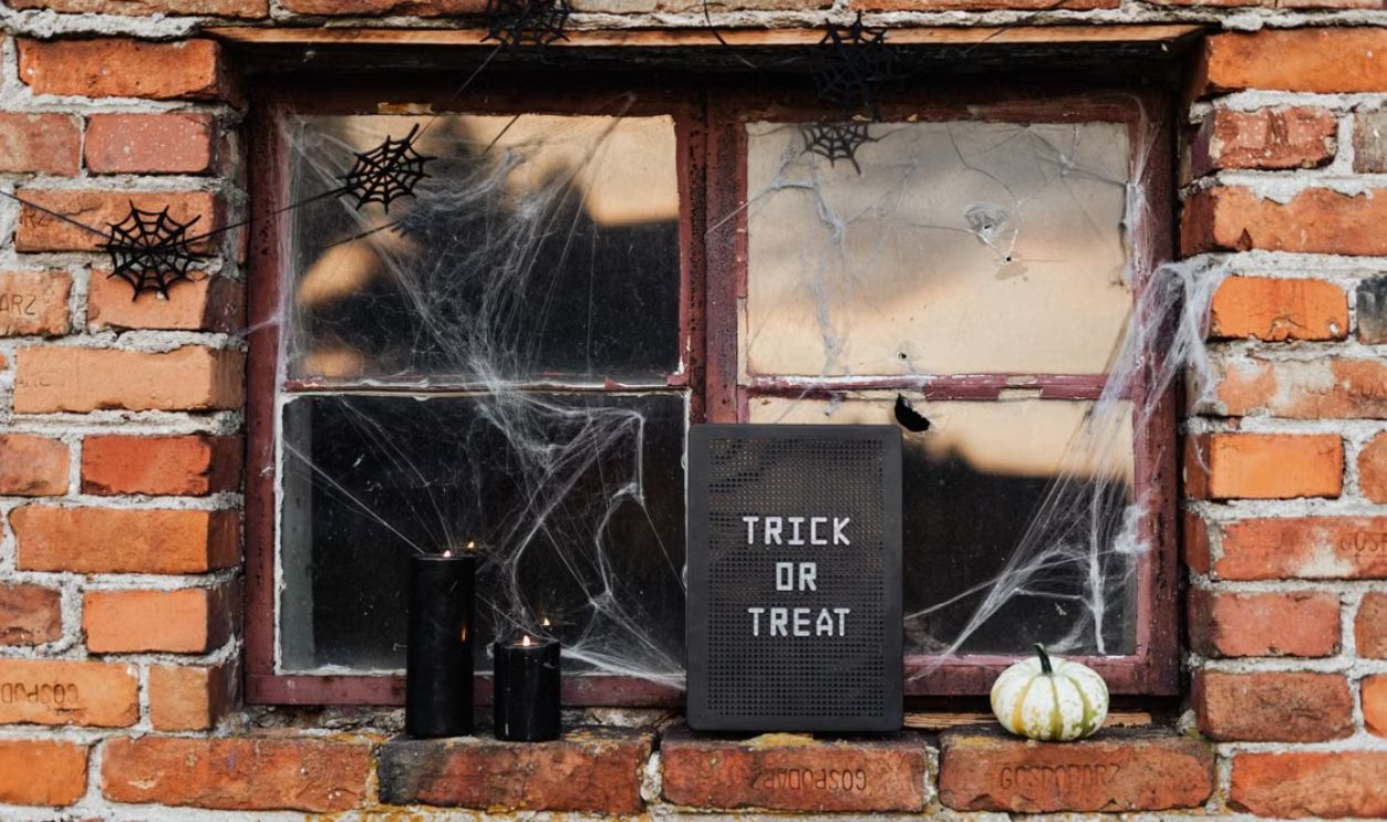 Spooky Halloween window decor with trick or treat sign, candles, and cobwebs.