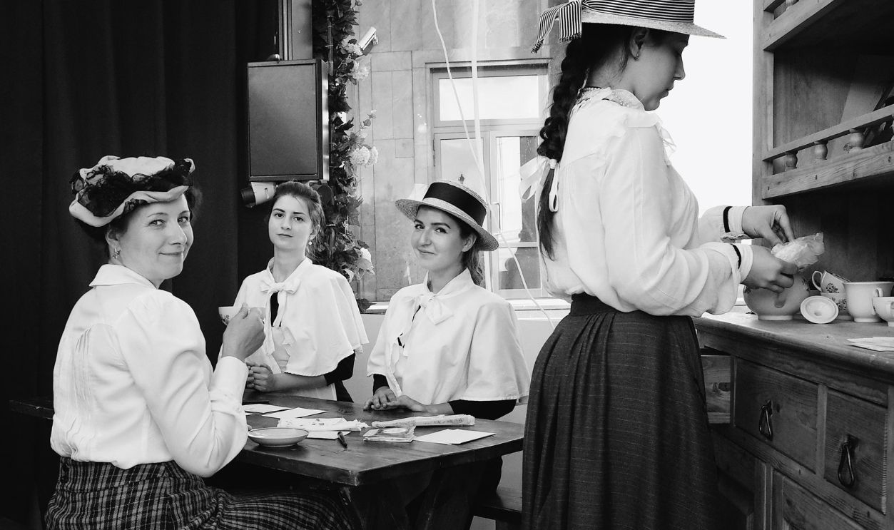 Four women in traditional clothing enjoying a vintage-style indoor tea party