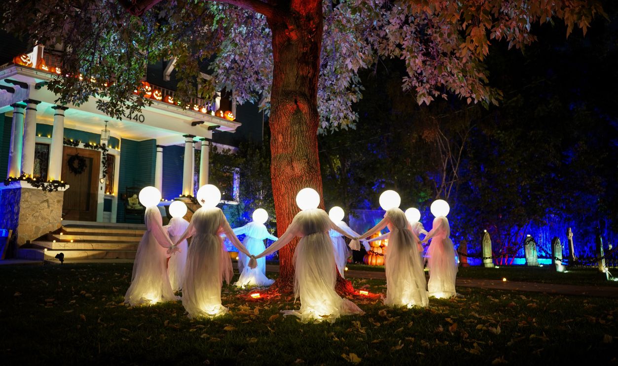 Eerie Halloween display featuring illuminated ghost decorations under a tree at night in a suburban yard