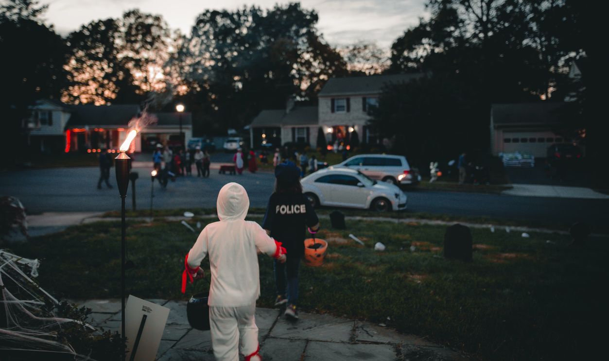 Children dressed in Halloween costumes trick-or-treating in a neighborhood at dusk, celebrating the festive spirit