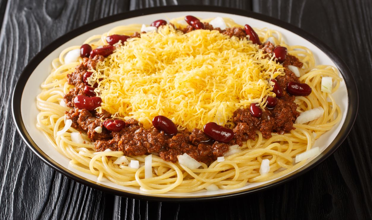 Delicious Cincinnati chili with spaghetti, cheddar cheese, fresh onions and beans close-up in a plate on the table. horizontal
