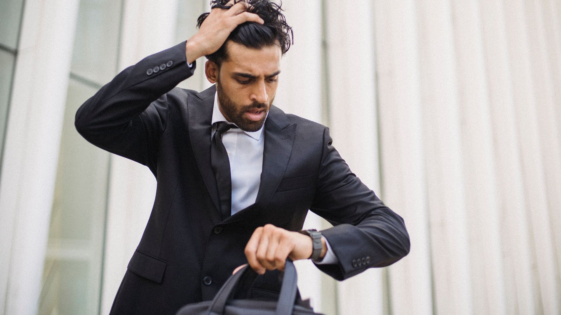 A businessman in a suit checks his watch, expressing stress. Suitable for business themes.