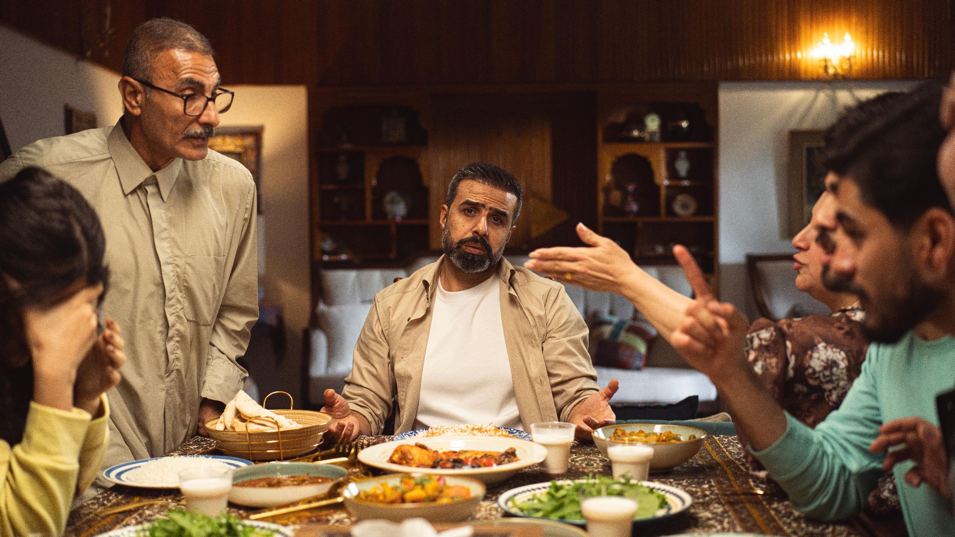 A family engages in a lively discussion around a dinner table filled with dishes.