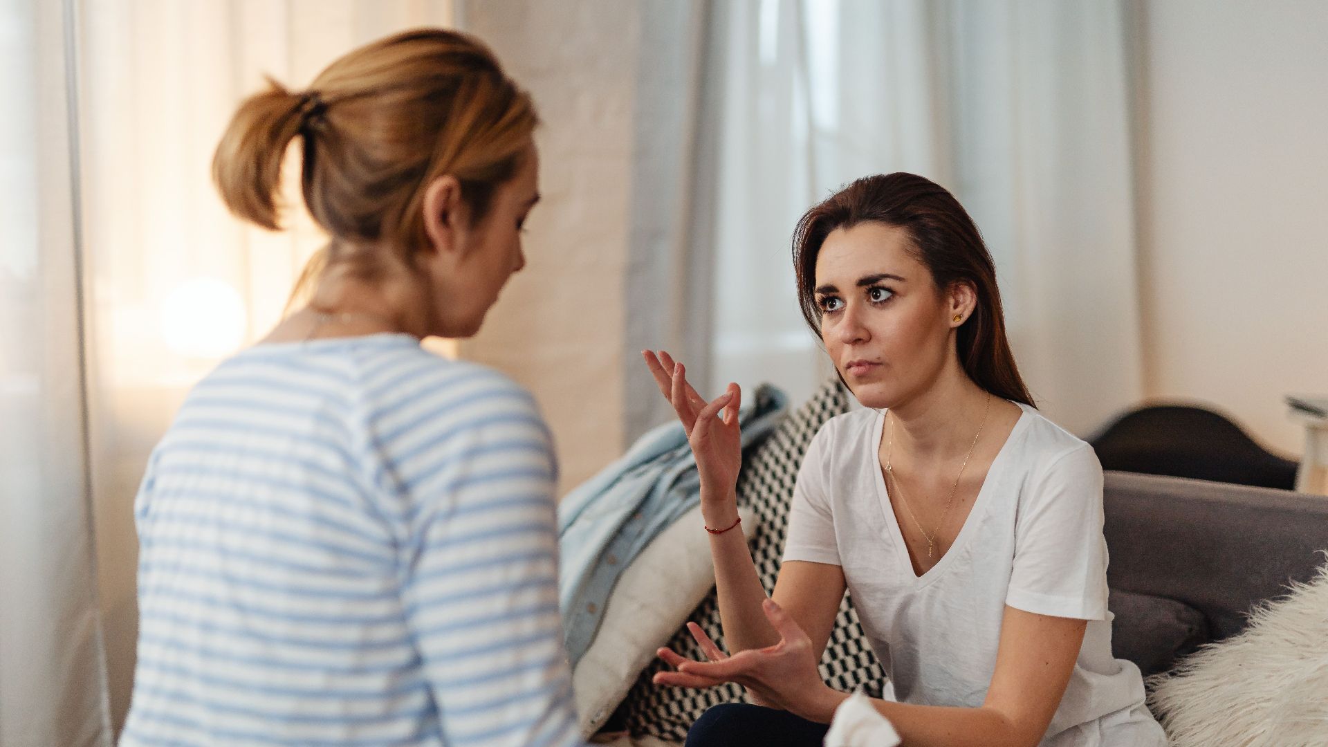 Two women sitting on a sofa, engaged in a serious discussion at home.