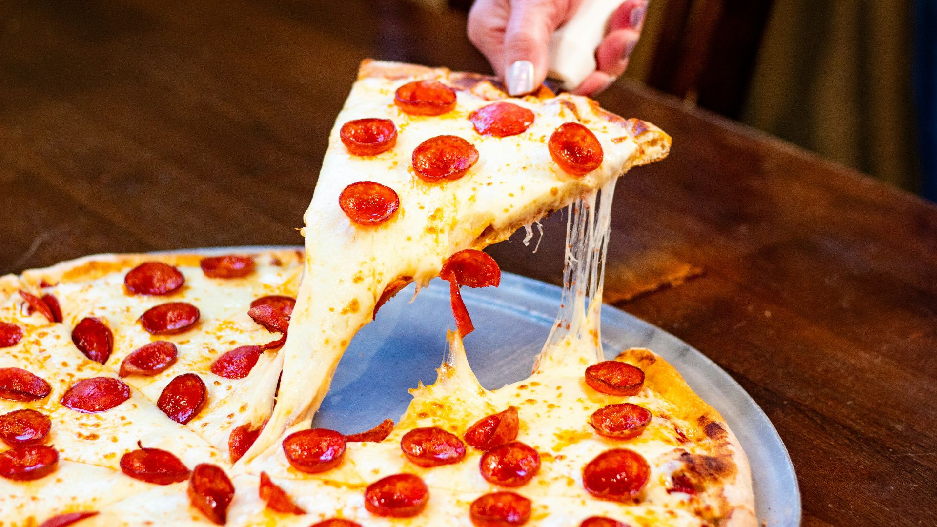 A hand lifts a cheesy slice of pepperoni pizza