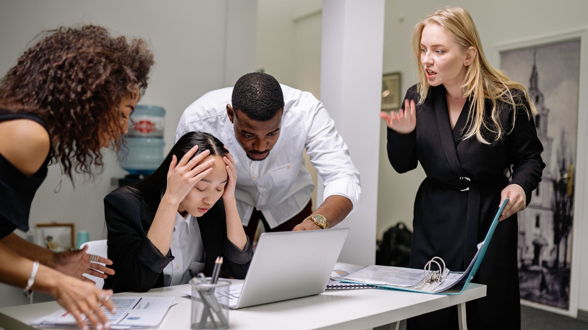 Group of diverse colleagues in an office engaged in a heated discussion around a laptop.