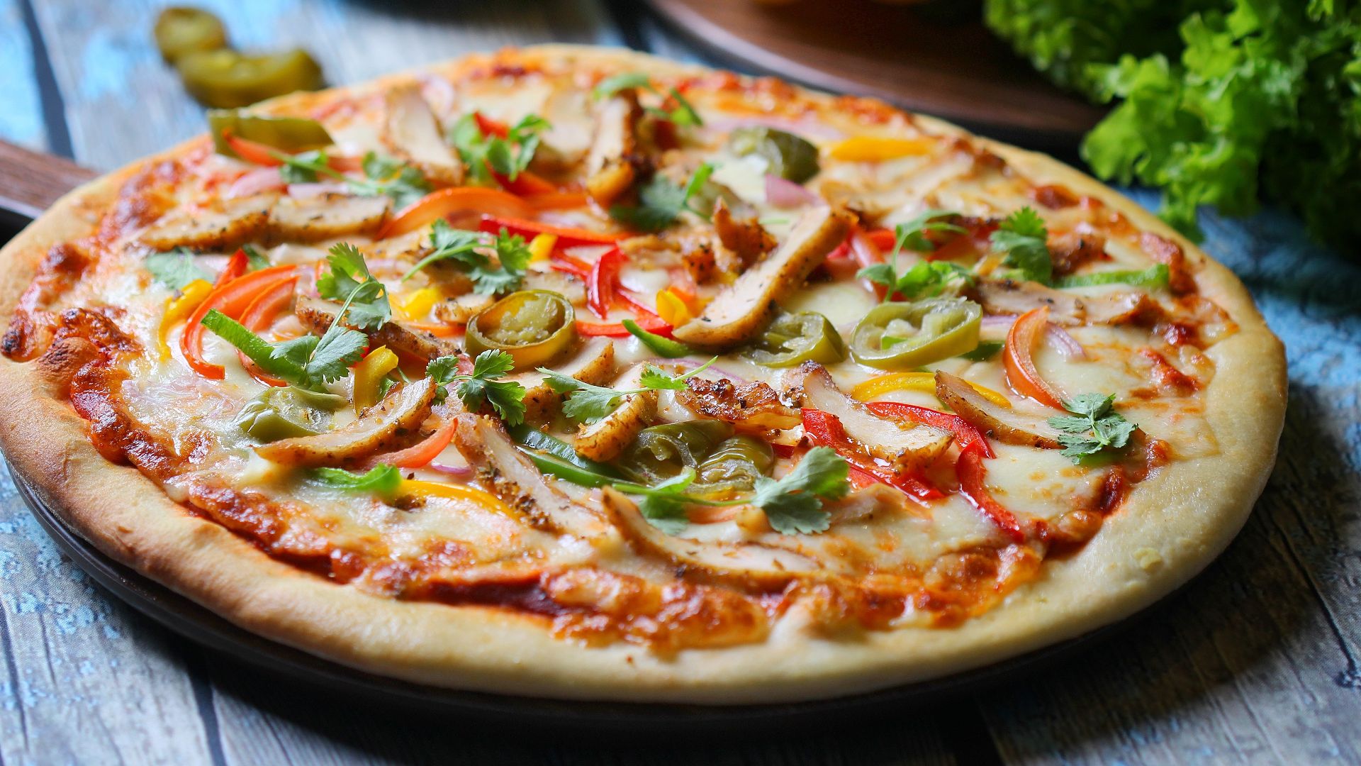 Delicious chicken pizza topped with vegetables on a wooden surface.