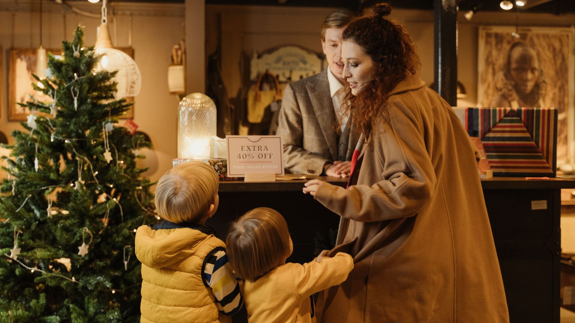 Family enjoying holiday shopping at a decorated store with a Christmas tree and sale offer.