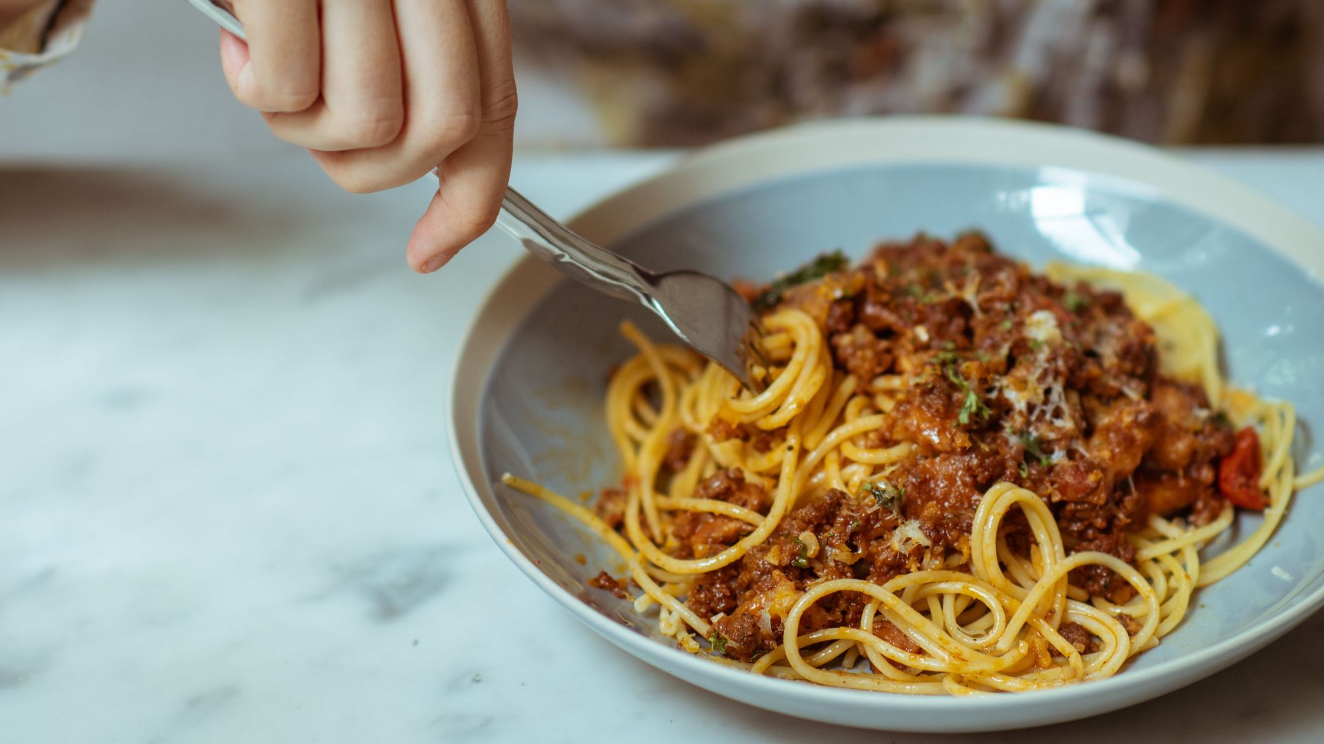 From above crop smiling brunette in stylish blouse sitting at marble table and enjoying delicious yummy spaghetti Bolognaise