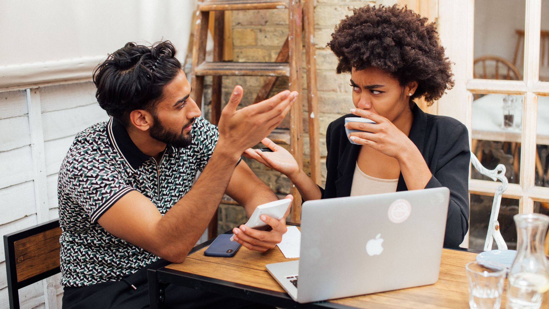 Two colleagues having a discussion while working on a laptop in an office space.