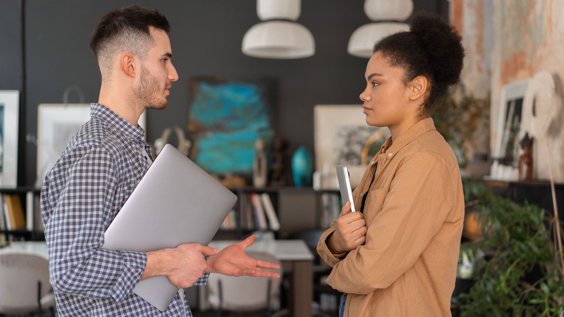 Two office workers engaged in a conversation, holding devices, in a modern office setting.
