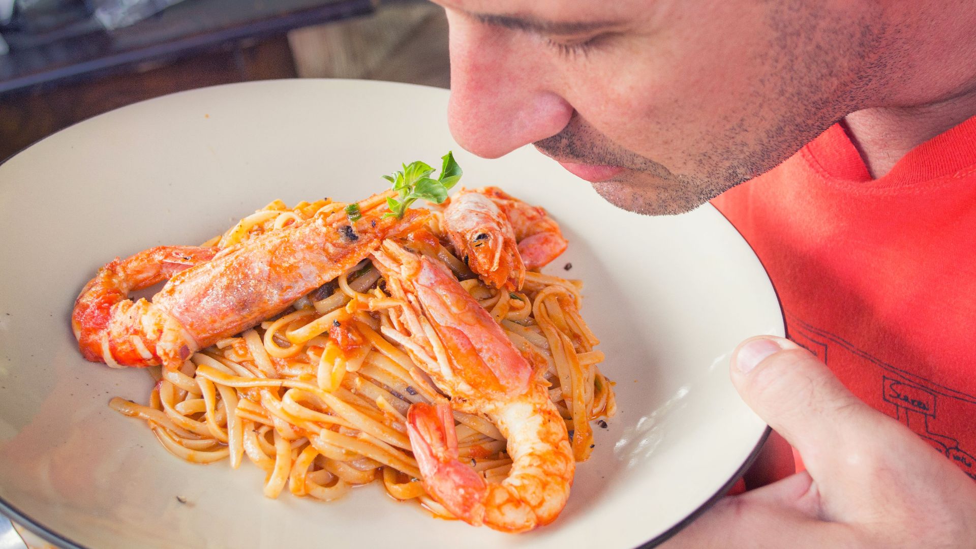 A man enjoys the aroma of a shrimp pasta dish with herbs. Perfect for food lovers.