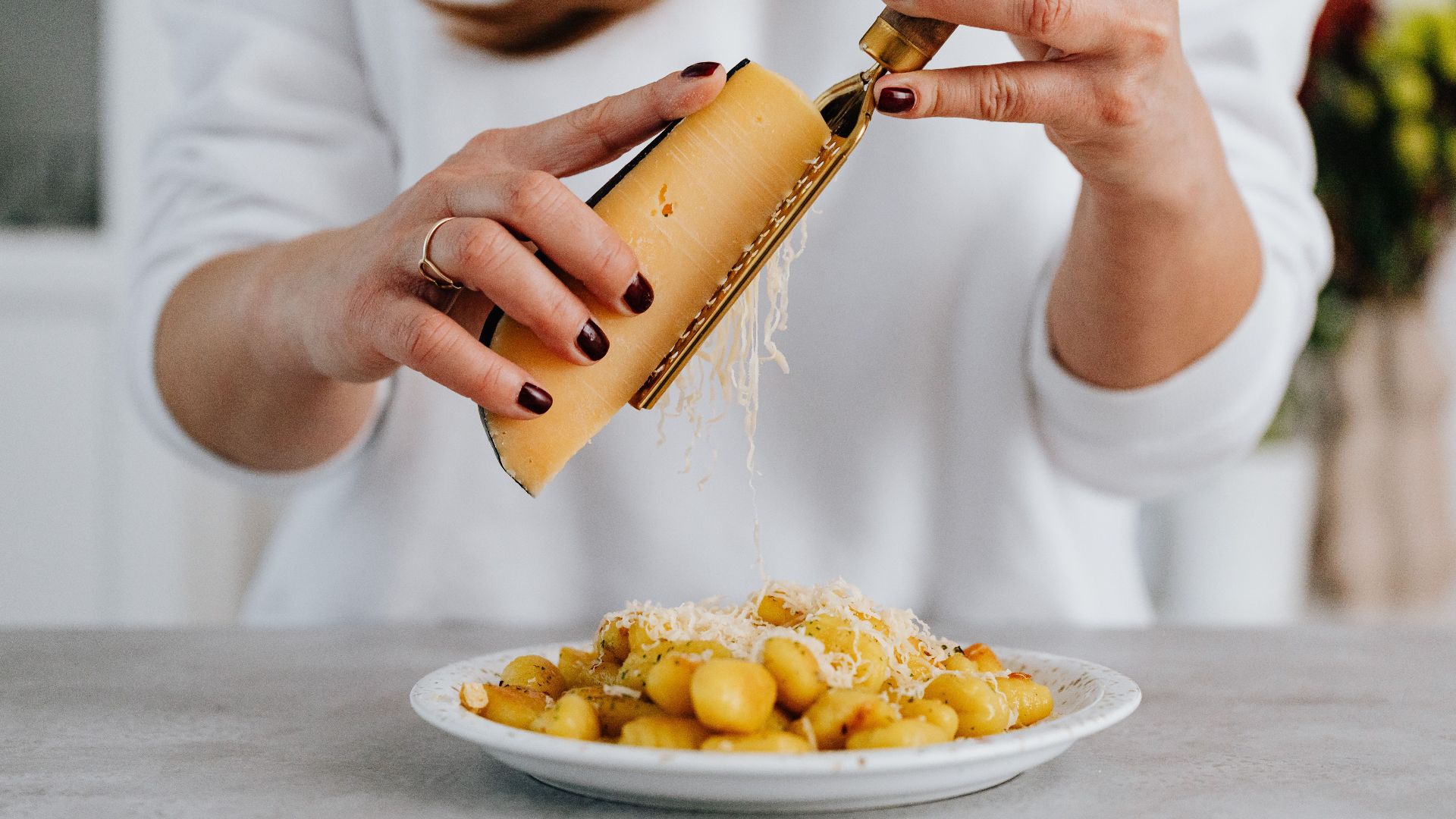 Close-up of Parmesan cheese being grated onto delicious gnocchi meal indoors.