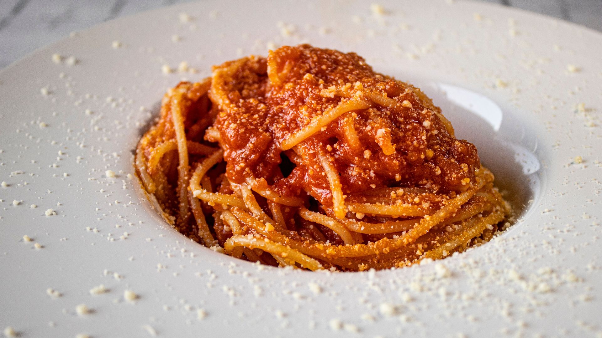 Appetizing spaghetti topped with rich tomato sauce and sprinkled with Parmesan, served on a ceramic plate.