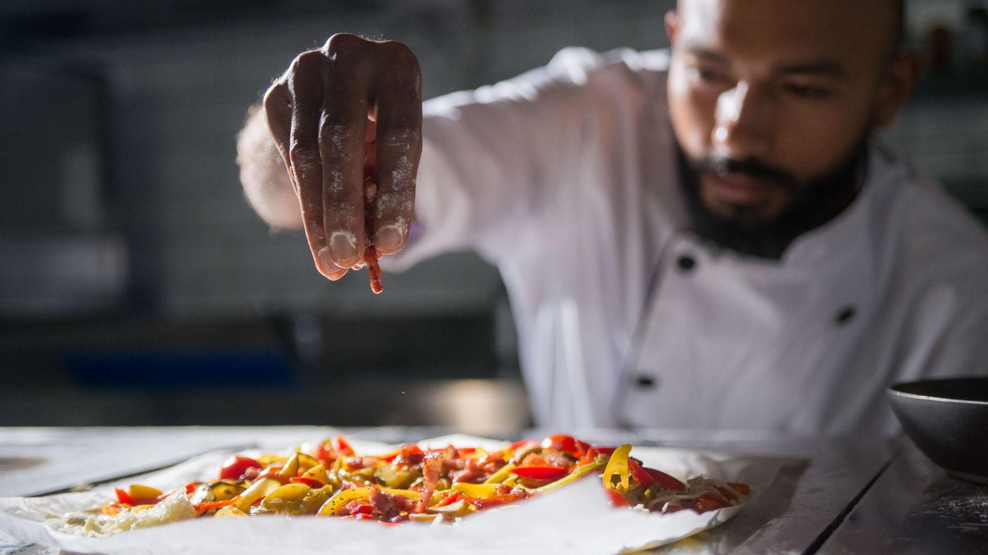 Professional chef skillfully preparing a vibrant homemade pizza with fresh ingredients.