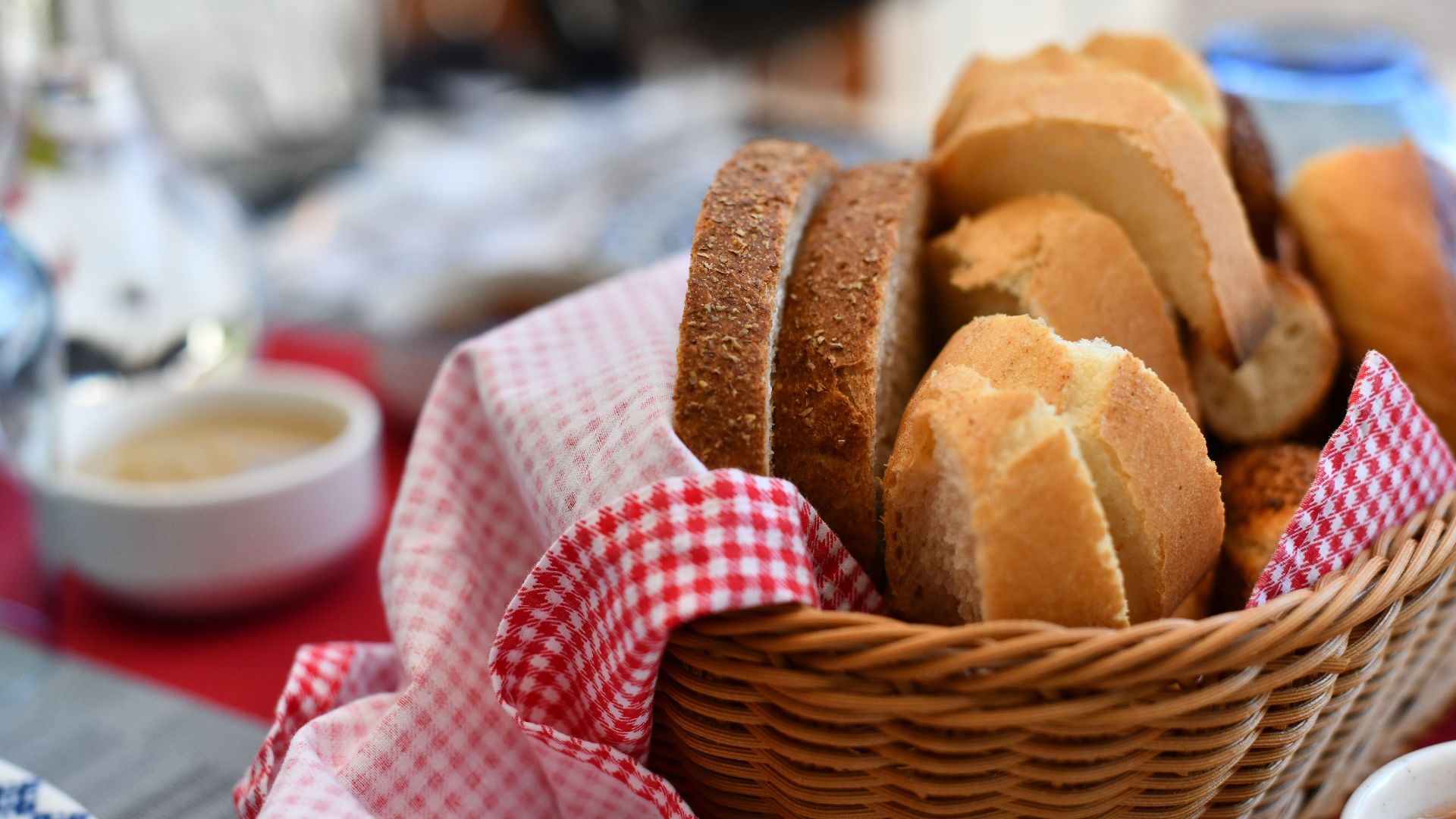 Assorted bread rolls in a wicker basket with red gingham cloth, perfect for breakfast.