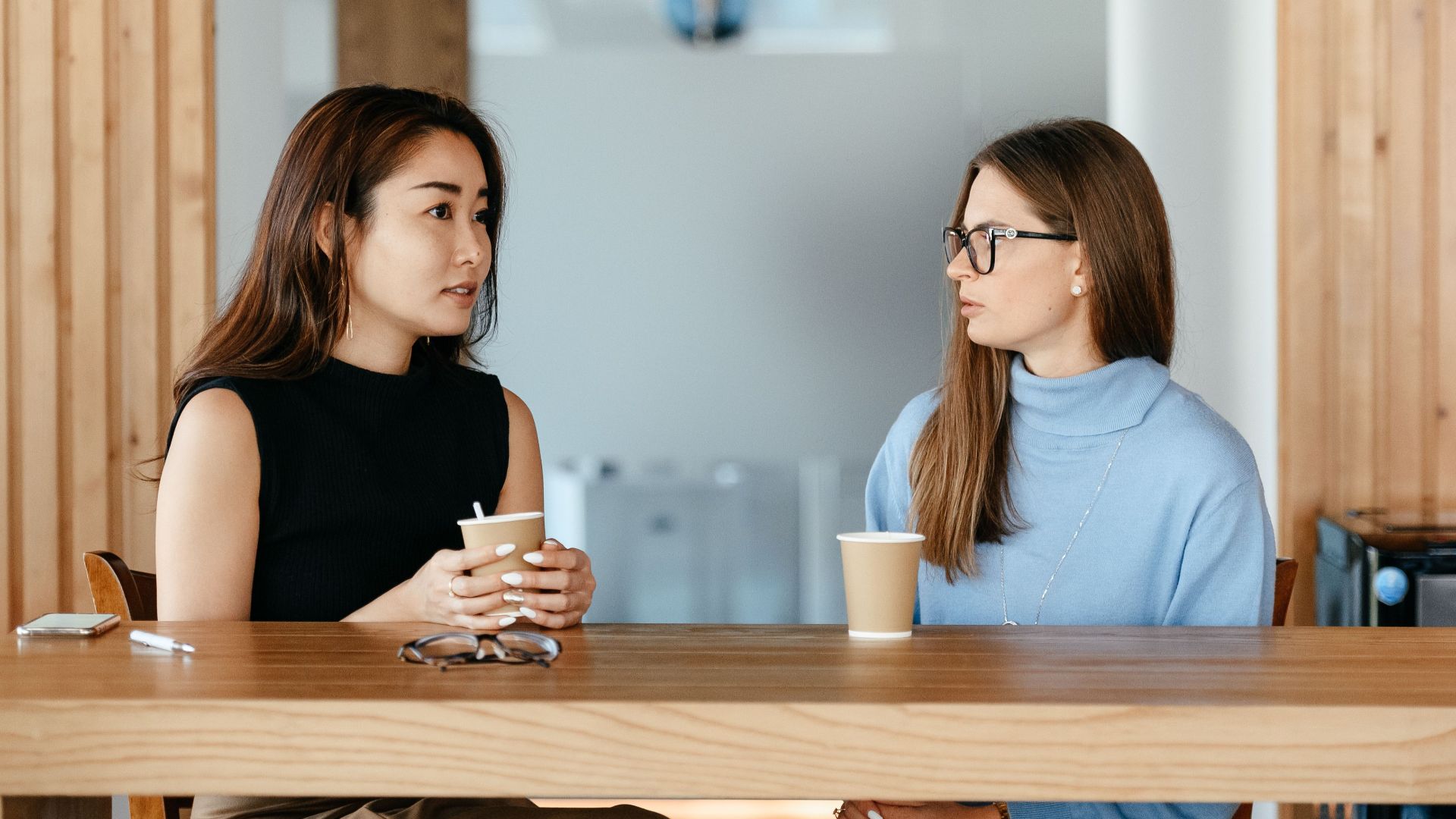 Young multiracial friends speaking at wooden table with cups of hot coffee in cafe