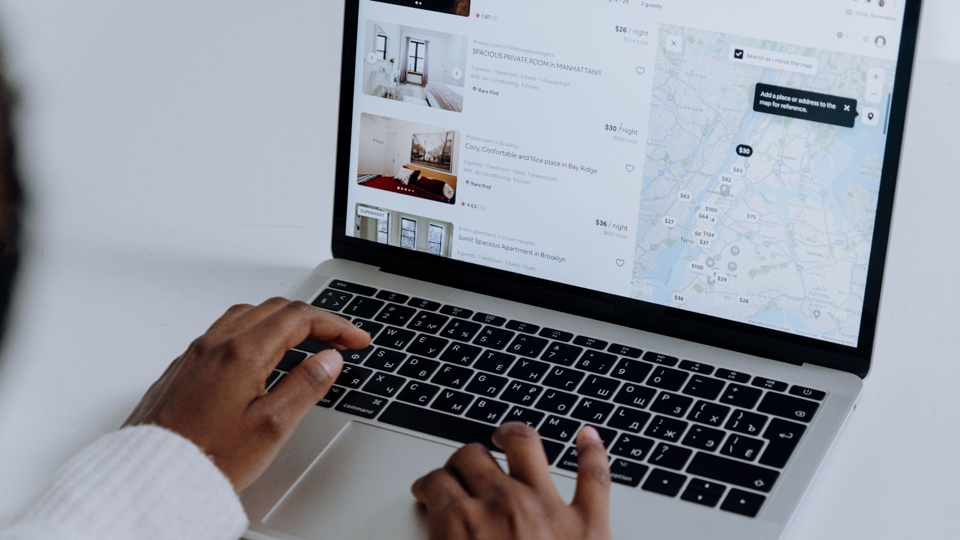 Hands typing on laptop searching Airbnb for accommodation options with map view.