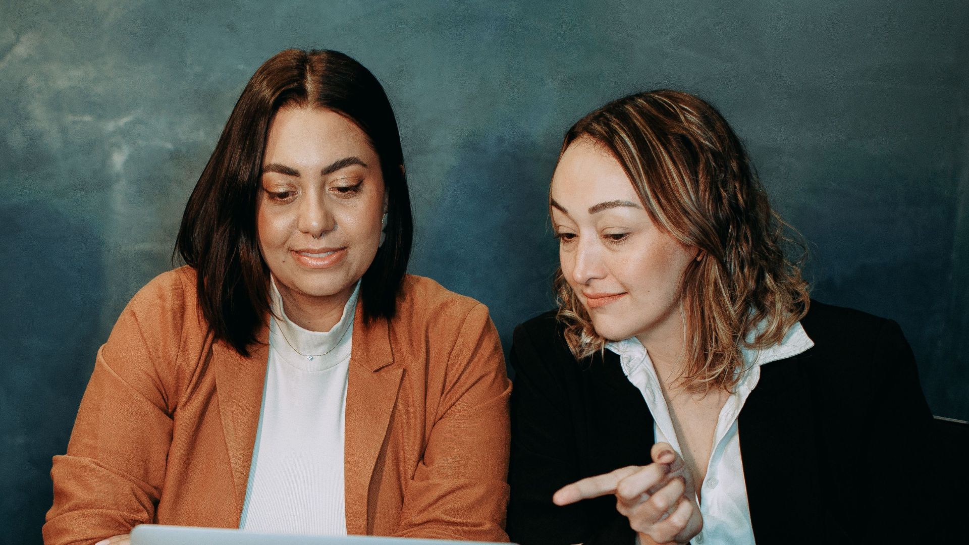 Three women working together on a laptop, discussing a project in a professional setting.