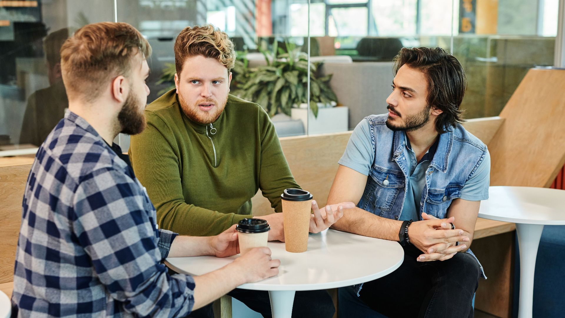 Three men having a casual business meeting in a cafe, engaging in conversation over coffee.
