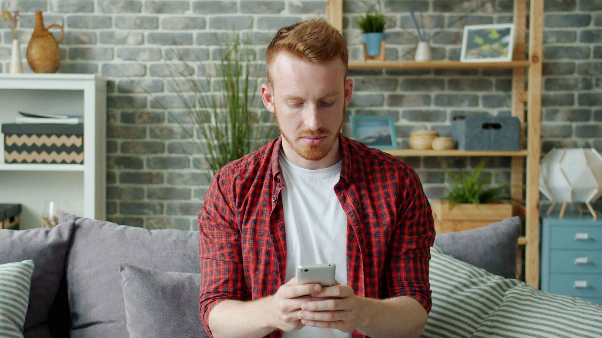 Young man in casual attire sitting on sofa using a smartphone indoors.